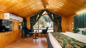 Una habitación de cabaña acogedora con techo de madera, una cama con cubrecama floral, dos sillas, una mesita y una ventana con cortinas.