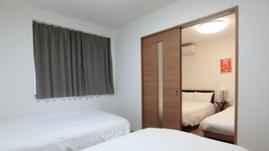 Een hotelkamer met twee enkele bedden, een houten garderobe, een spiegel, een nachtkastje met een lamp en een raam met gordijnen.