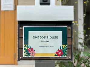 A sign for eRapos House in Imamiya, featuring a wooden frame and floral design.