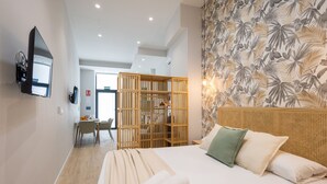 Une chambre d’hôtel avec un lit, un téléviseur fixé au mur, une cloison en bois et un mur orné d’un motif de feuilles.