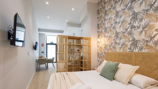 Ein Hotelzimmer mit Bett, Wandfernseher, einer Holzwand und einer Wand mit Blätermotiv.