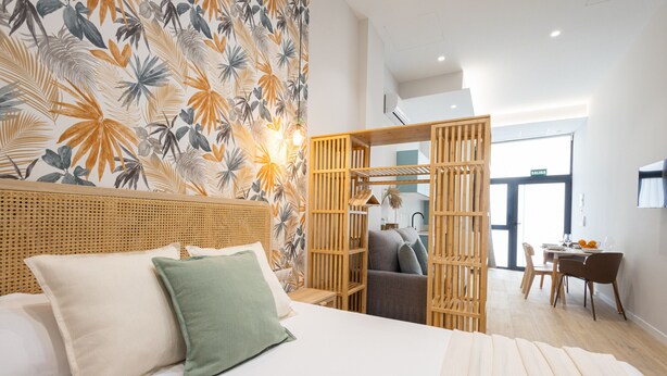 Ein Schlafzimmer mit Bett, Kissen, einem Holzkopfteil, einer Wand mit tropischen Blättern, einer Holzwand und einem Schreibtisch mit Stuhl.