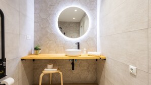 Ein modernes Badezimmer mit Waschtisch aus Holz, einem runden Spiegel und einer Rückwand aus sechseckigen Fliesen.