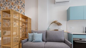 Ein Wohnzimmer mit grauem Sofa, einer Holzbibliothek und einer Küchenzeile mit Türkis-Schränken.