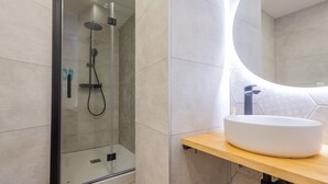Une salle de bain moderne avec une douche à parois de verre, un miroir rond et un lavabo blanc posé sur un plan de travail en bois.
