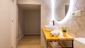 Ein modernes Badezimmer mit einem Holzbadezimmerkorpus, einem weißen Waschbecken, einem Spiegel und einer kleinen Topfpflanze.