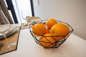 Taula amb una cistella de filferro que conté taronges, un got de vi i un plat.