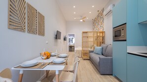 Eine moderne Küche mit Mikrowelle, ein Essbereich mit Tisch für zwei Personen und ein graues Sofa.