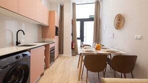 Une cuisine compacte dotée d’appareils électroménagers modernes, un coin repas avec une table dressée pour deux personnes, et une vue à travers une porte.