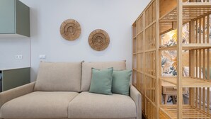 Ein beiges Sofa mit zwei grünen Kissen, ein Holzregal und zwei gewebte Wanddekorationen.