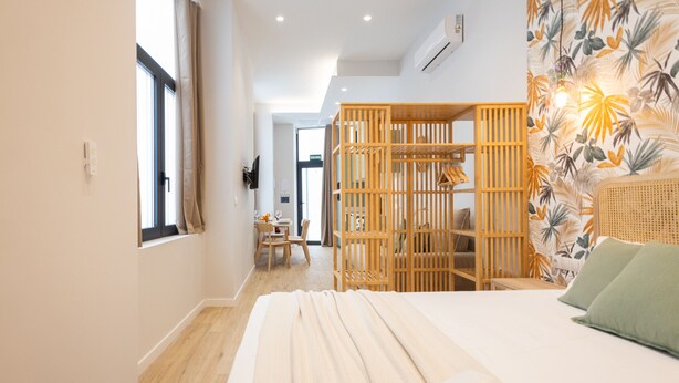 Ein Schlafzimmer mit einem Bett, einer Holzwand, einem Korbstuhl und einer Wand mit einem tropischen Blattmuster.