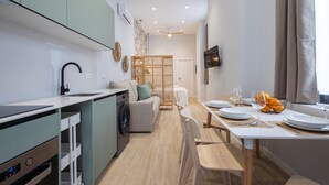 Eine moderne Küche mit integriertem Waschmaschine, eine Essecke mit Tisch für zwei Personen und ein Wohnbereich mit Sofa und Wand-Fernseher.