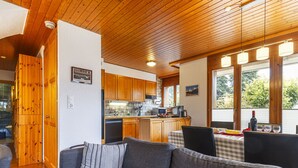 A cozy living area with a sofa, a dining table with chairs, wooden cabinets, and a kitchen area with a sink and stove. - Pavillons A by Interhome (Champery)