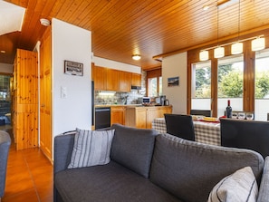 Ein gemütlicher Wohnbereich mit einer Couch, einem Esstisch mit Stühlen, Holzschränken und einer Küchenzeile mit Spüle und Herd.