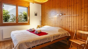 A wooden-paneled room with a bed, a chair, a window, and a wall-mounted light fixture. - Pavillons A by Interhome (Champery)