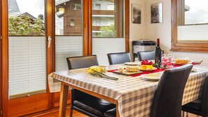 A dining area with a checkered tablecloth, wooden chairs, a printer, and a bottle of wine. - Pavillons A by Interhome (Champery)