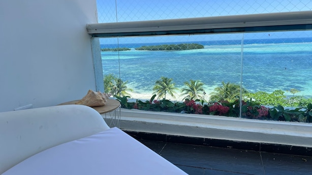 A room with a large window overlooking a beach and turquoise waters. - Aquamarine Retreat Penthouse Boca Chica (Boca Chica)