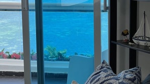 A room with a large sliding glass door leading to a balcony overlooking a turquoise sea and a lush green landscape. - Aquamarine Retreat Penthouse Boca Chica (Boca Chica)