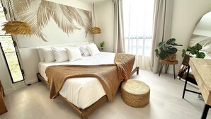 A modern bedroom with a wooden bed, white bedding, a woven throw blanket, and a round wicker stool. - NEW- Expansive Ocean View- Pool/Tennis/Pickleball (Waikoloa Village)