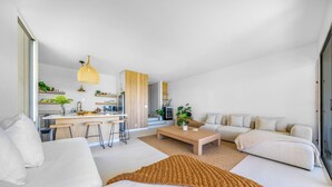 A modern living room with a sofa, coffee table, and a kitchen area in the background. - NEW- Expansive Ocean View- Pool/Tennis/Pickleball (Waikoloa Village)