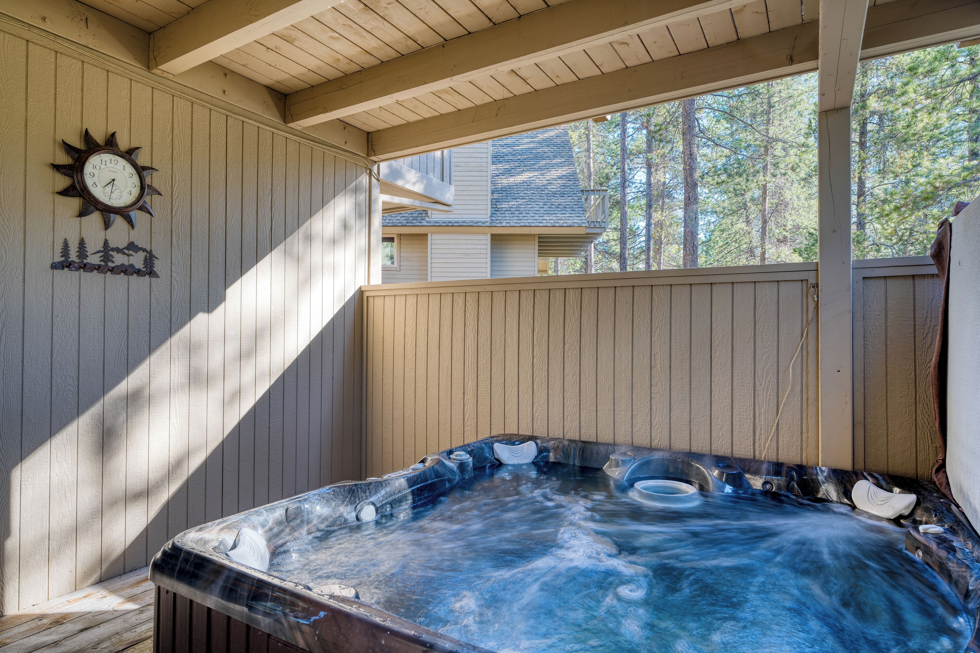 Un bain à remous installé sur une terrasse en bois, agrémentée d’une horloge et d’un élément décoratif mural.