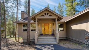 A two-story house with a front porch, wooden steps, and a front door. - Quail by AvantStay | Great Location + Game Room, Hot Tub, & Deck! (Sunriver)