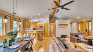 A spacious kitchen with wooden cabinets, a dining area with a long table, and a leather sofa in a well-lit room with a ceiling fan. - Quail by AvantStay | Great Location + Game Room, Hot Tub, & Deck! (Sunriver)