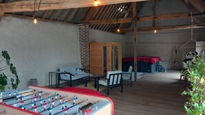 An indoor space with a foosball table, wooden beams, a brick wall, and a hanging light fixture. - Discover the Châteaux of the Loire (La Ferriere)