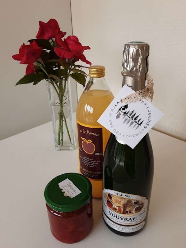 Una ampolla de vi Vouvray, una ampolla de suc de poma, un bocal de melmelada i un vas amb roses vermelles damunt d'un taulell.