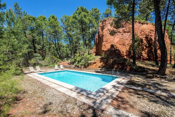 A rectangular swimming pool surrounded by a stone deck, with lounge chairs and a red rock formation in the background. - Agréable Havres de Paix à Roussillon (Roussillon)