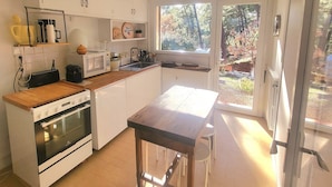 Una cocina con armarios blancos, encimera de madera, estufa, microondas y ventana con vistas a un jardín.