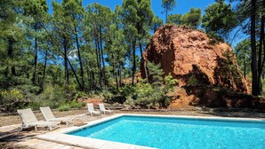 Una piscina con sillones de descanso, rodeada de árboles y una gran formación rocosa.
