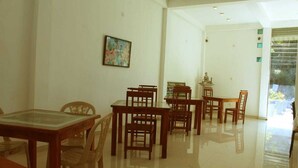 A dining area with wooden tables and chairs, a glass-top table, and a painting on the wall. - Thirasara Holiday Resort (Thissamaharama)