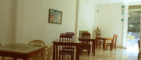 Un comedor con mesas y sillas de madera, una mesa con cubierta de vidrio y un cuadro en la pared.