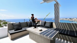 A modern outdoor seating area with a concrete bench and cushions, overlooking a coastal view. - Design Superior Suite with Clear Sea View, Shared Infinity Pool, Gym, Pool Bar (C965+8J Mykonos, Greece)