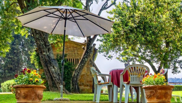 An outdoor seating area with a table and chairs, a large umbrella, and potted plants. - Montaione Charm: Spacious Haven (Montaione)