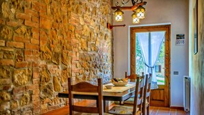 A rustic dining area with a stone wall, wooden chairs, a table with a bowl, and a door leading outside. - Montaione Charm: Spacious Haven (Montaione)