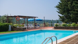 A swimming pool with lounge chairs and umbrellas, surrounded by a brick deck and greenery. - Apartment in Tuscany with Pool & Garden (Montaione)