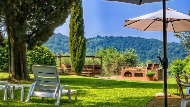 A garden with outdoor seating, a pergola, and a brick structure with a chimney. - Apartment in Tuscany with Pool & Garden (Montaione)