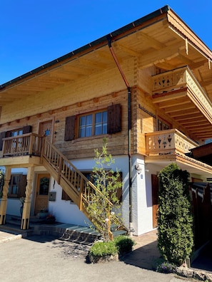 Un bâtiment en bois doté d’un balcon, d’un escalier et d’un petit arbre au premier plan.