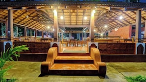 An outdoor covered seating area with wooden benches and tables, a central staircase, and a view of the surrounding landscape. - Lazo Areca Resort (Madikeri)