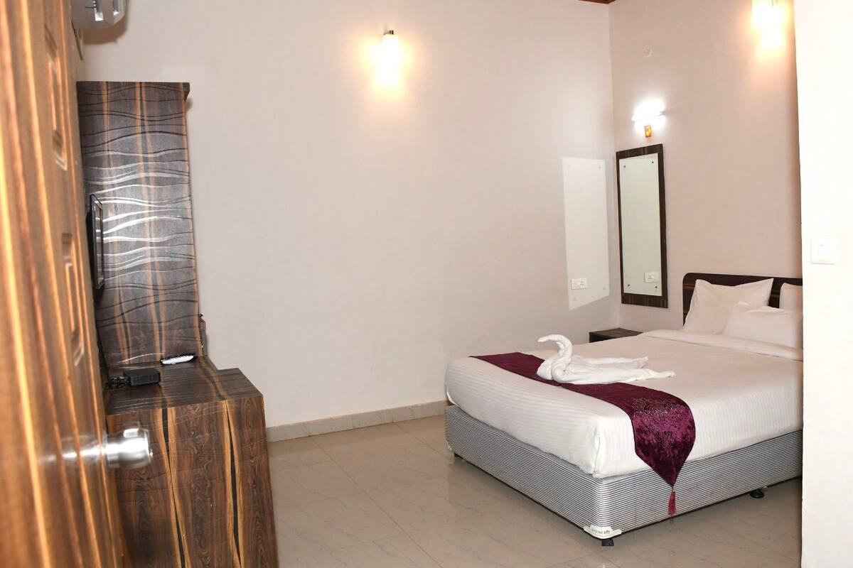 A hotel room with a bed, a wooden dresser, a mirror, and a wall-mounted light fixture.