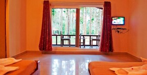 Quarto de hotel com duas camas, televisão e varanda com mesa e cadeiras.