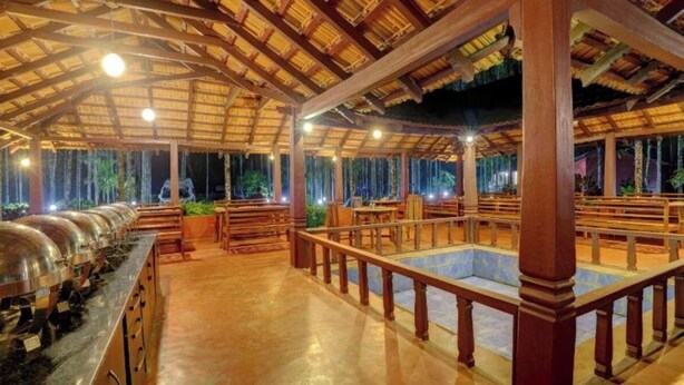 A covered outdoor dining area with a long counter, multiple tables, and a central pool. - Lazo Areca Resort (Madikeri)
