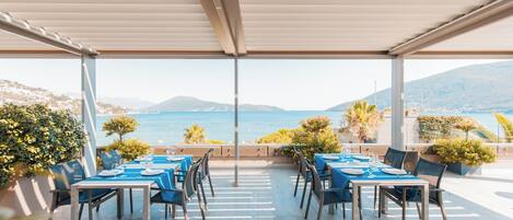 Un área de comedor al aire libre con mesas y sillas, con vista a un paisaje costero.
