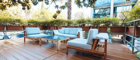 An outdoor patio with wooden flooring, a blue sofa, a wooden chair, and a glass table.