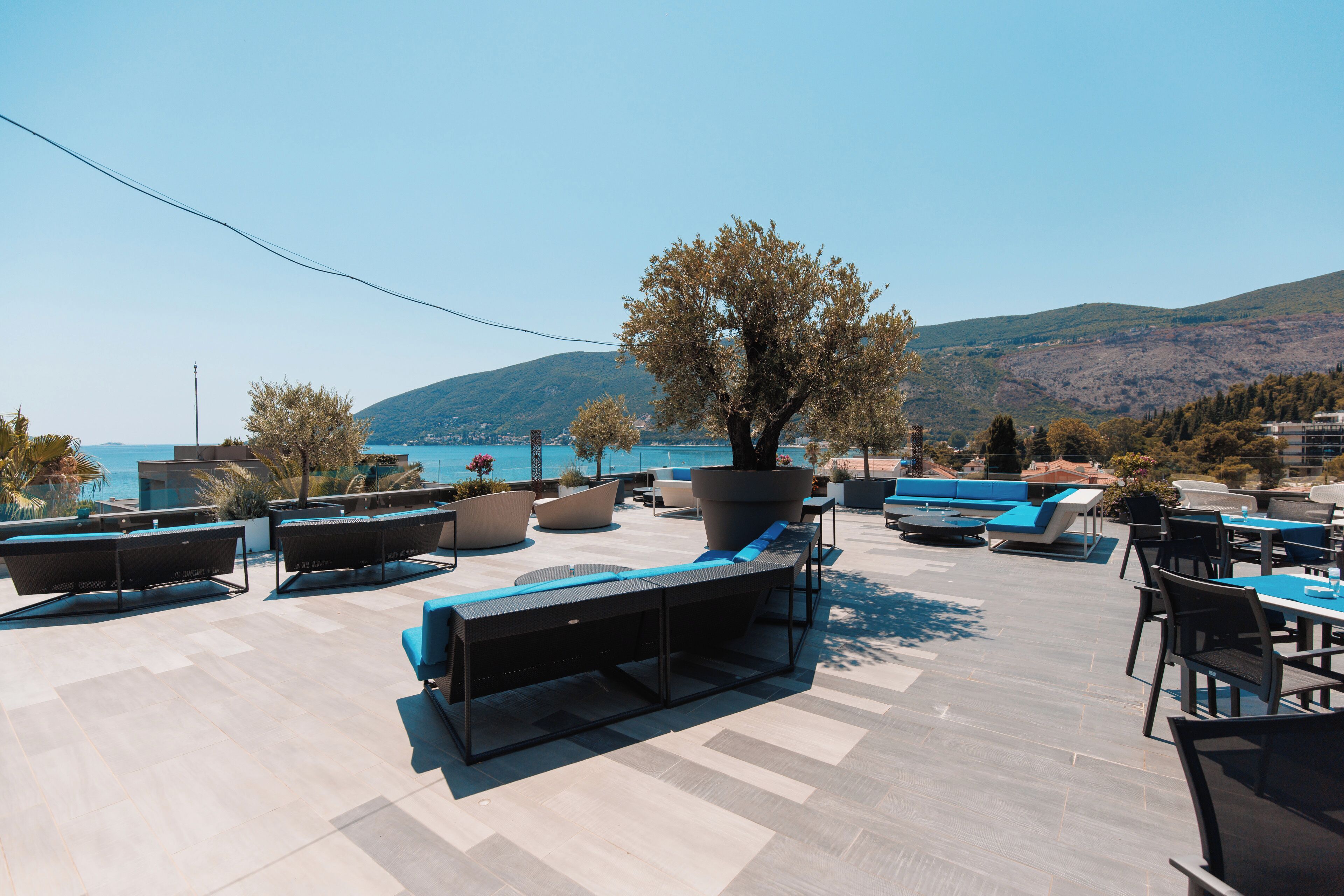 An outdoor seating area with lounge chairs and tables, overlooking a body of water and hills.