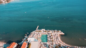 An aerial view of a coastal resort with a swimming pool, beach umbrellas, and a pier extending into the sea. - Palmon Bay Hotel & Spa (Igalo)