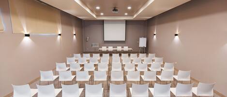 A conference room with rows of white chairs, a projector screen, and a whiteboard.