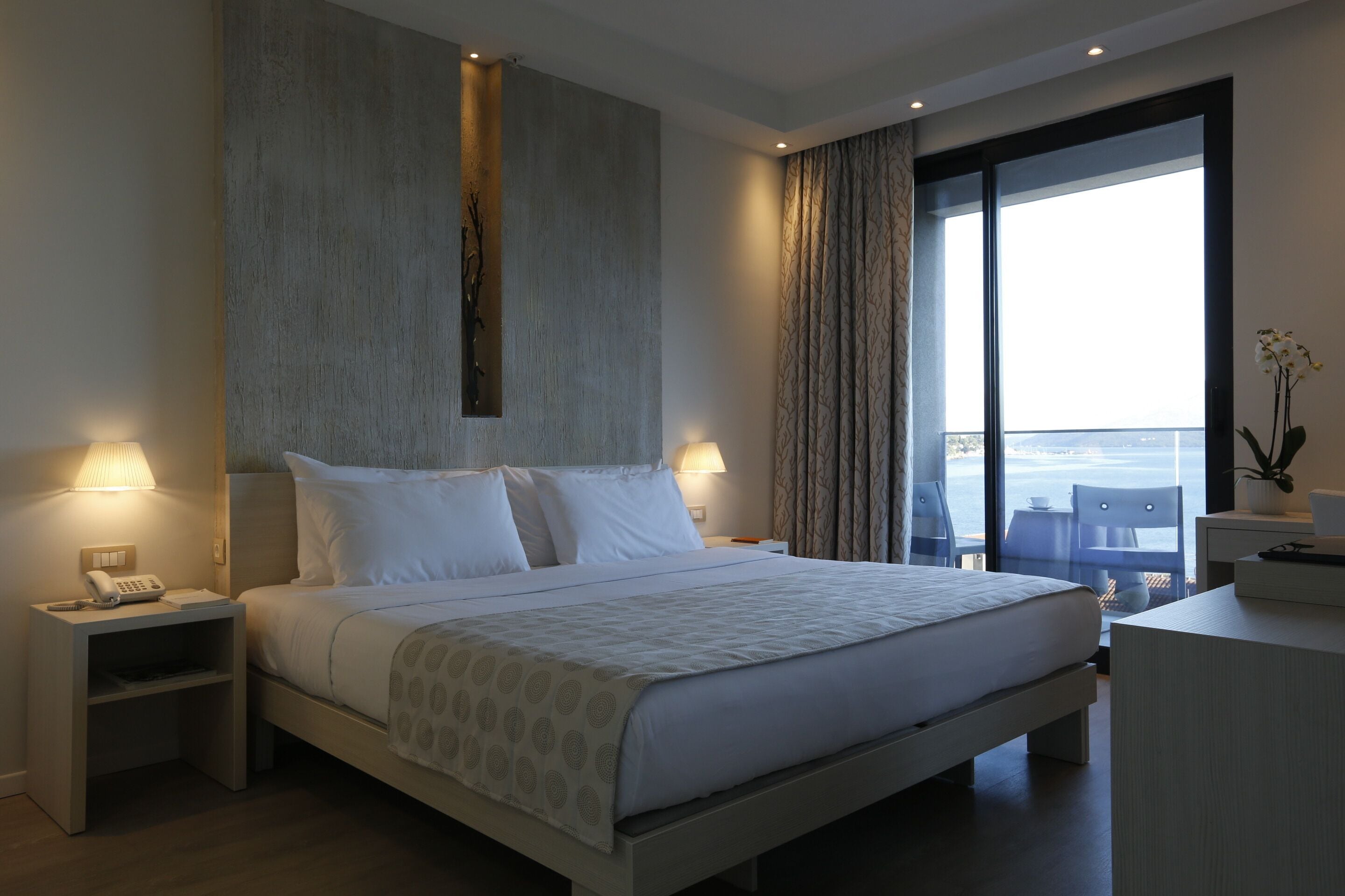 Une chambre d’hôtel moderne, dotée d’un grand lit, de lampes de chevet, d’une table de chevet, d’un bureau et offrant une vue sur la ville grâce à de grandes fenêtres.